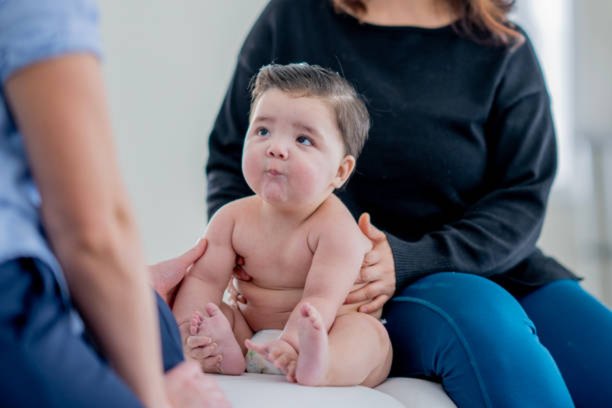 Baby sitting supported during a physiotherapy assessment with a parent close by